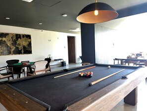 A pool table with balls, chairs, and a hanging light fixture in a room with a large window and a map on the wall. - Beachfront 2-Bedroom Condo, Ocean and Island Views, Jacuzzi – Mazatlán (Mazatlán)
