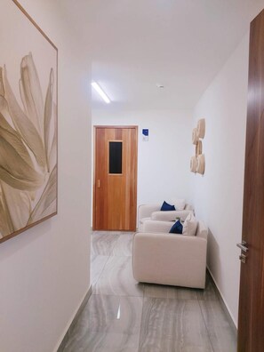 A hallway with a wooden door, a white sofa with blue cushions, and a large abstract painting on the wall. - Beachfront 2-Bedroom Condo, Ocean and Island Views, Jacuzzi – Mazatlán (Mazatlán)