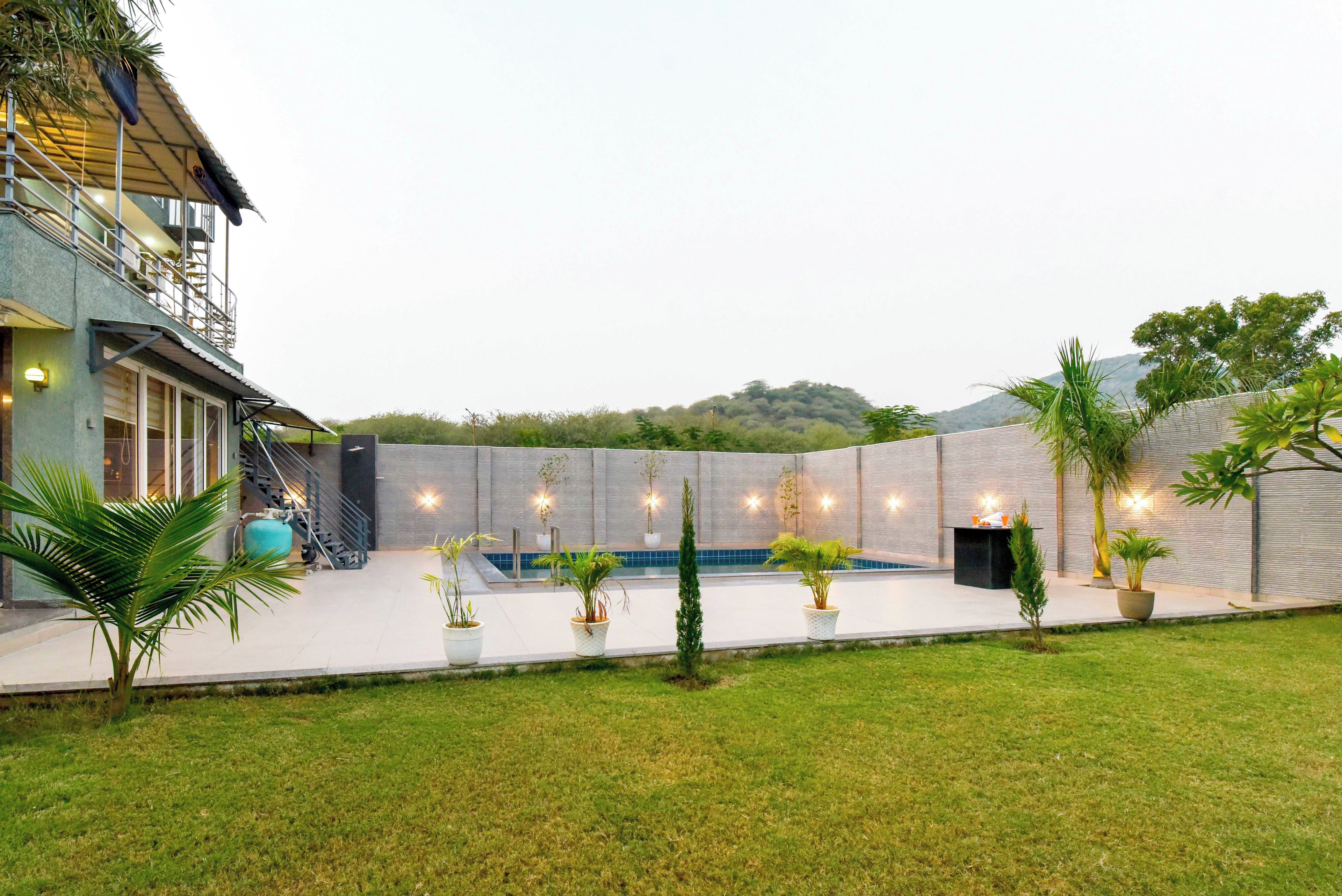 A residential backyard with a swimming pool, potted plants, and a staircase leading to a balcony.