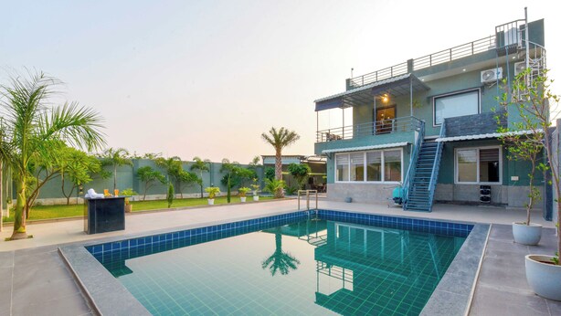 A modern two-story building with a swimming pool, outdoor seating, and a well-maintained garden. - DanCenter Hill's Stay Villa 3BHK (Kishangarh)