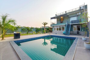 Un edificio moderno de dos plantas con piscina, asientos exteriores y un jardín bien cuidado.