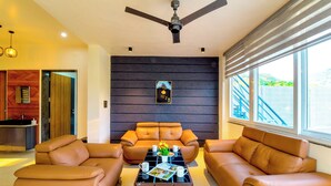 A modern living room with leather sofas, a coffee table, and a ceiling fan. - DanCenter Hill's Stay Villa 3BHK (Kishangarh)