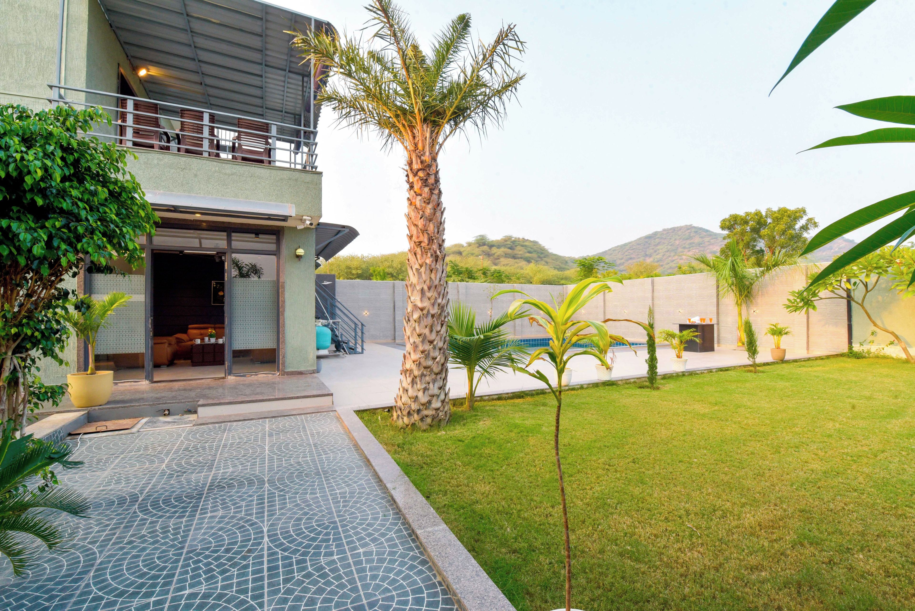 A modern building with a covered outdoor area, a palm tree, and a pool with a patterned floor.