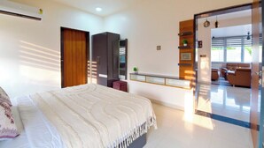 A modern bedroom with a large bed, a wardrobe, a built-in wardrobe, a small seating area, and a view of the outside. - DanCenter Hill's Stay Villa 3BHK (Kishangarh)