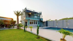 A modern two-story building with a swimming pool, surrounded by a well-maintained lawn and potted plants. - DanCenter Hill's Stay Villa 3BHK (Kishangarh)