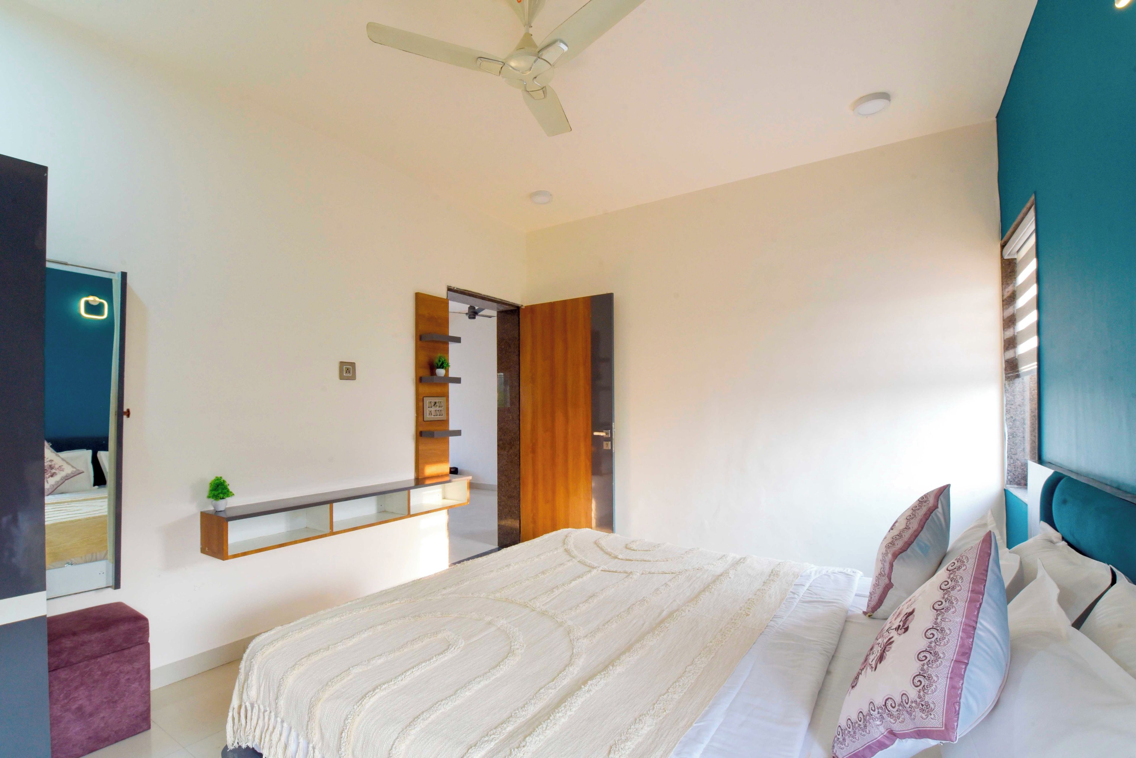 A bedroom with a bed, a ceiling fan, a bedside table, a mirror, and a door leading to another room.
