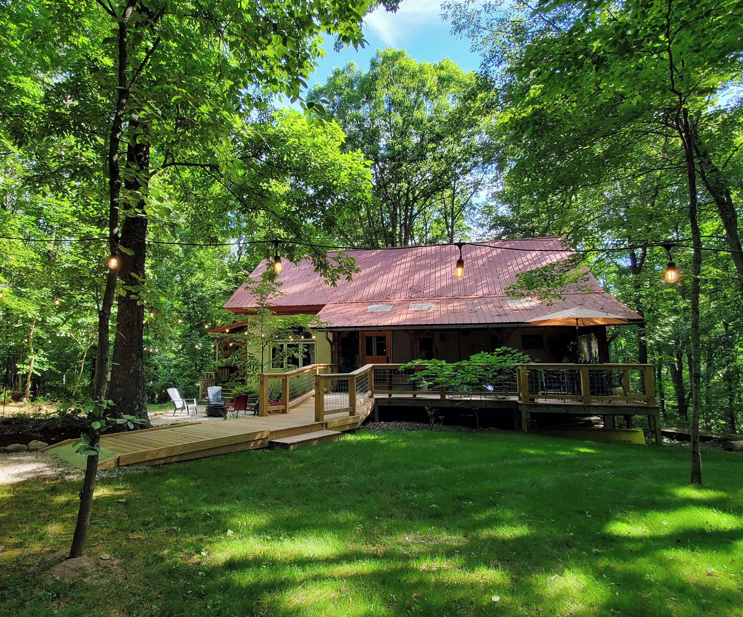 A rustic cabin with a wooden deck, surrounded by lush greenery.