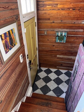 Ein Holzinnenraum mit einem Schachbrettfußboden, einer gelben Tür und einem gerahmten Bild an der Wand.
