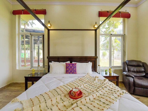 Un dormitorio con una cama, una silla y dos ventanas con cortinas.