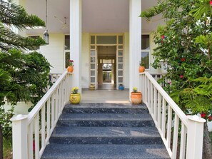 A staircase leading to a building entrance with a white railing, potted plants, and a clear view into the building.