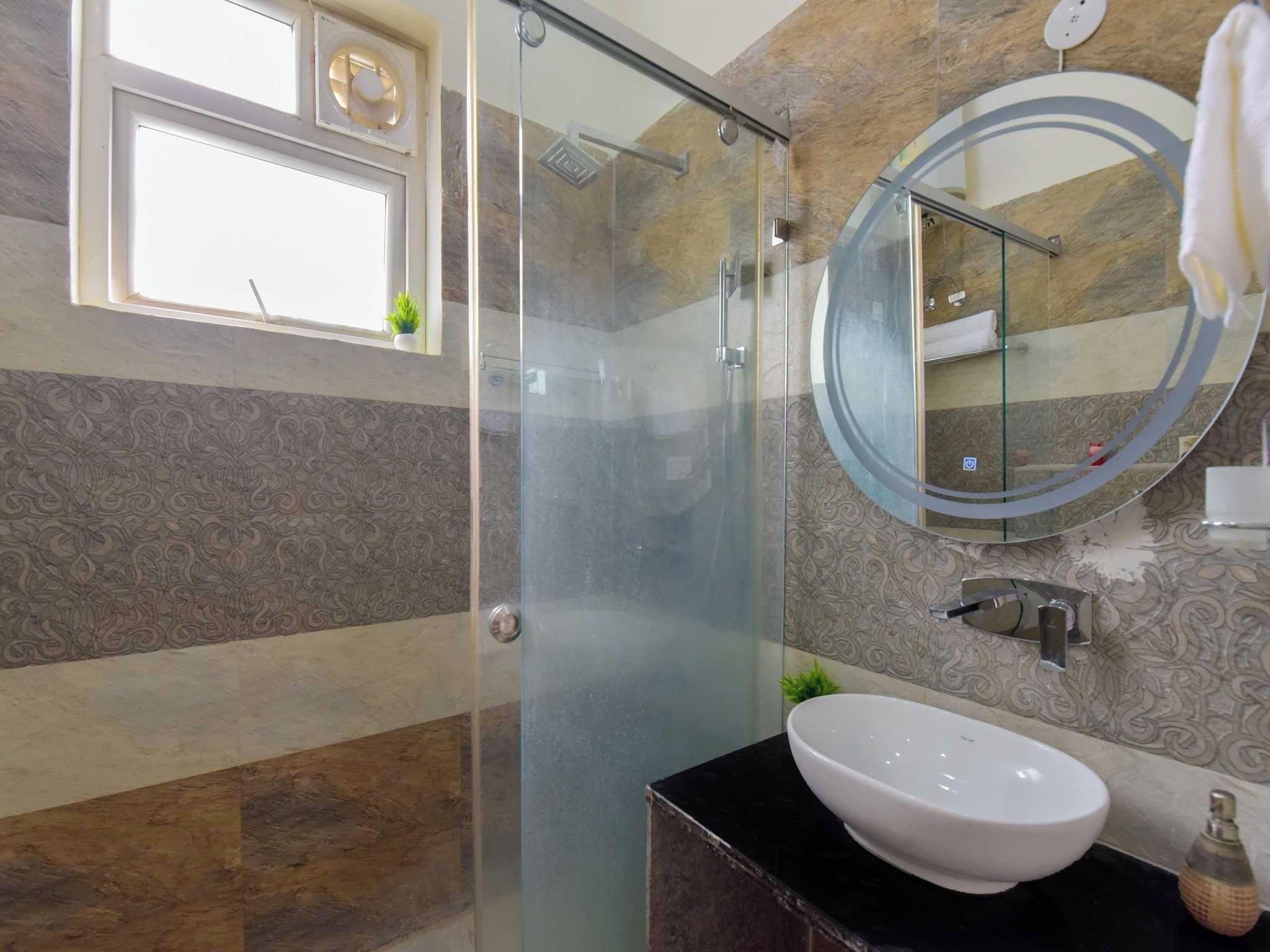 A bathroom with a glass-enclosed shower, a round mirror, and a white sink.