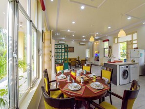A dining area with a table set for four, a kitchen with a washing machine, and a view of greenery outside.