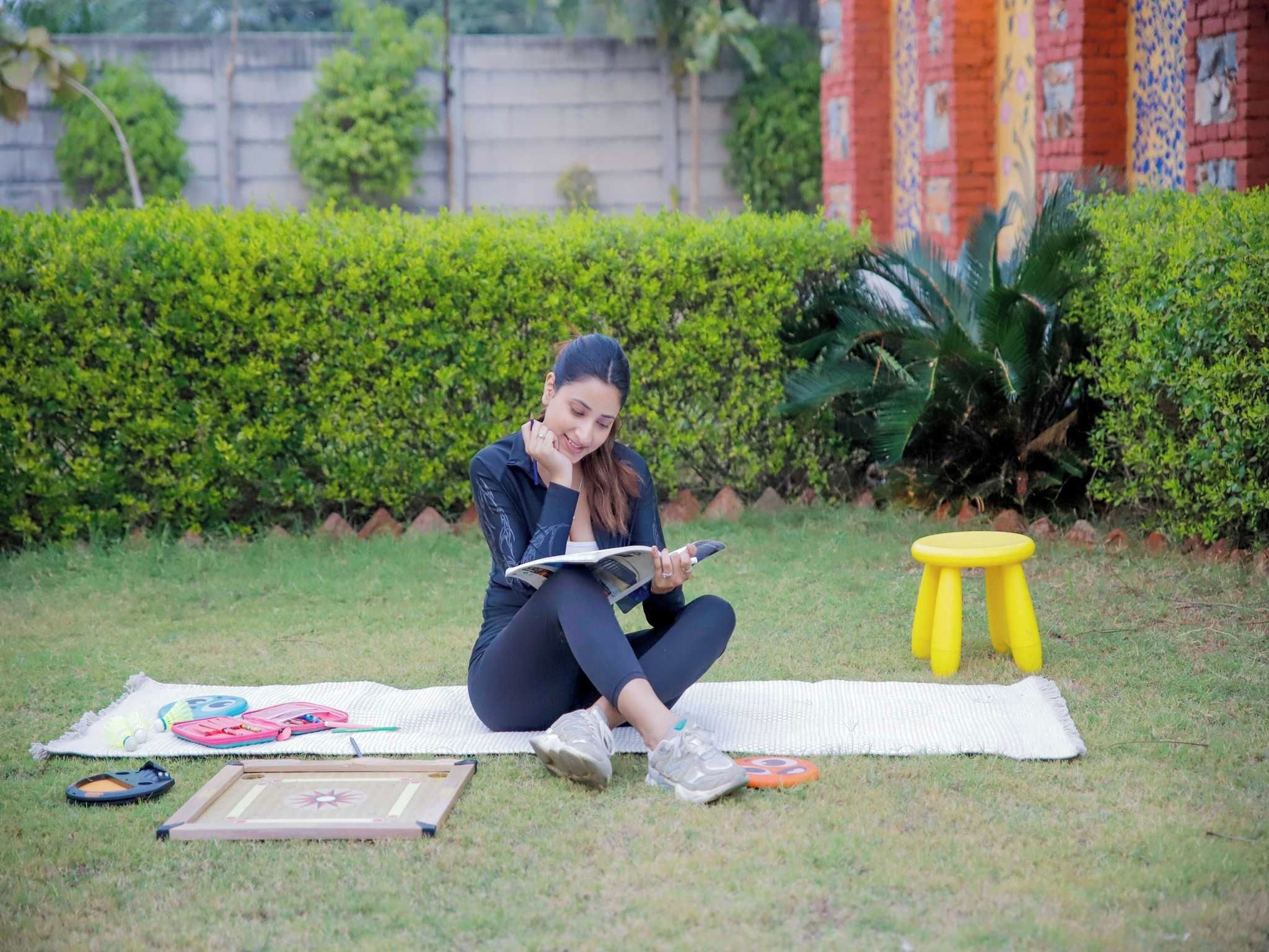 A person sitting on a mat outdoors with a book, a small stool, and a mat game.
