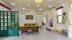 Uma sala de estar ampla com um sofá amarelo, cadeiras de madeira, um divisória verde com sinos pendurados e um ventilador de teto.