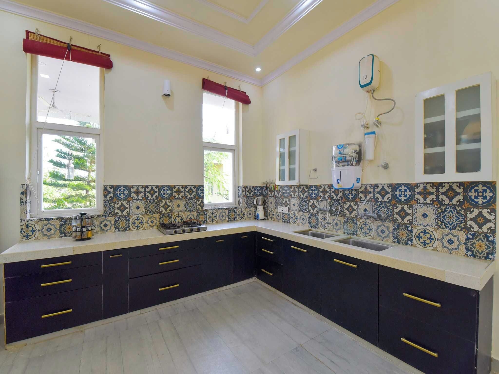 A kitchen with dark cabinets, a gas stove, a sink, and a window with a red curtain.