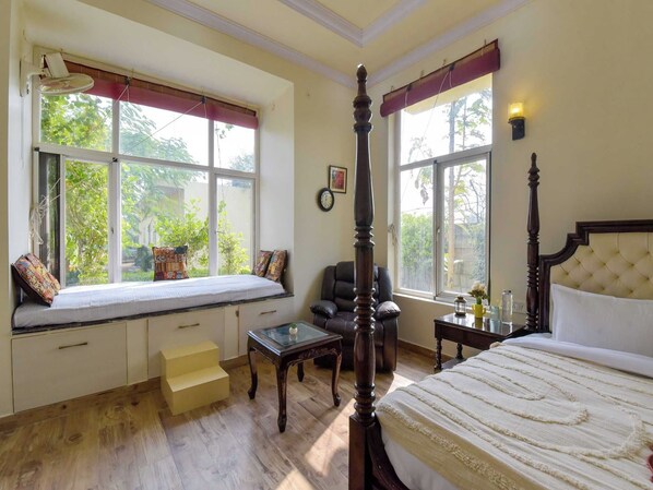 A bedroom with a four-poster bed, a window seat, a chair, and a bedside table.