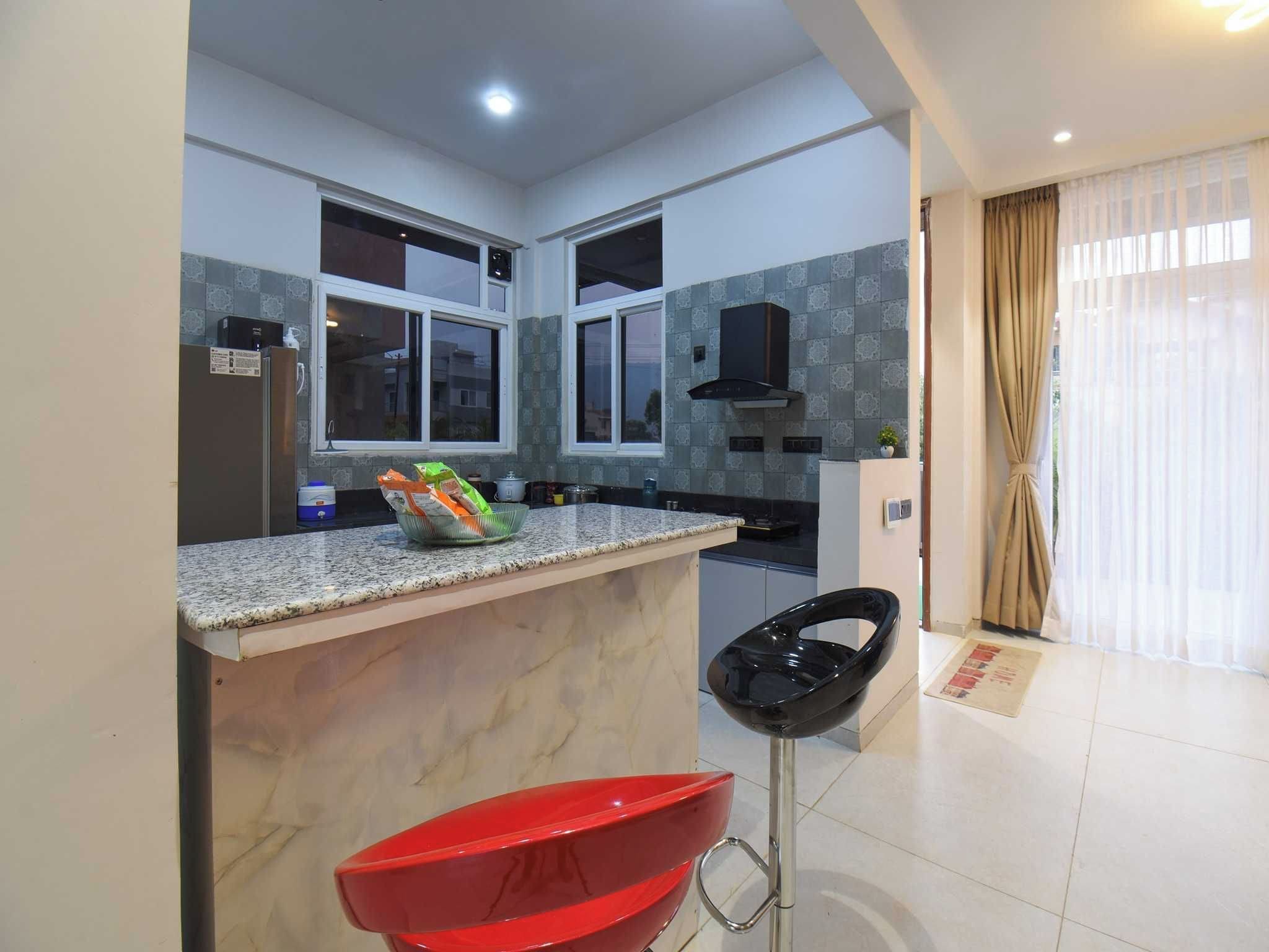 Una cocina moderna con encimeras de granito, un taburete rojo y una silla negra.