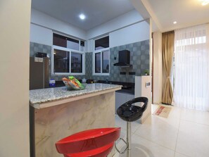 A modern kitchen with granite countertops, a red bar stool, and a black chair.