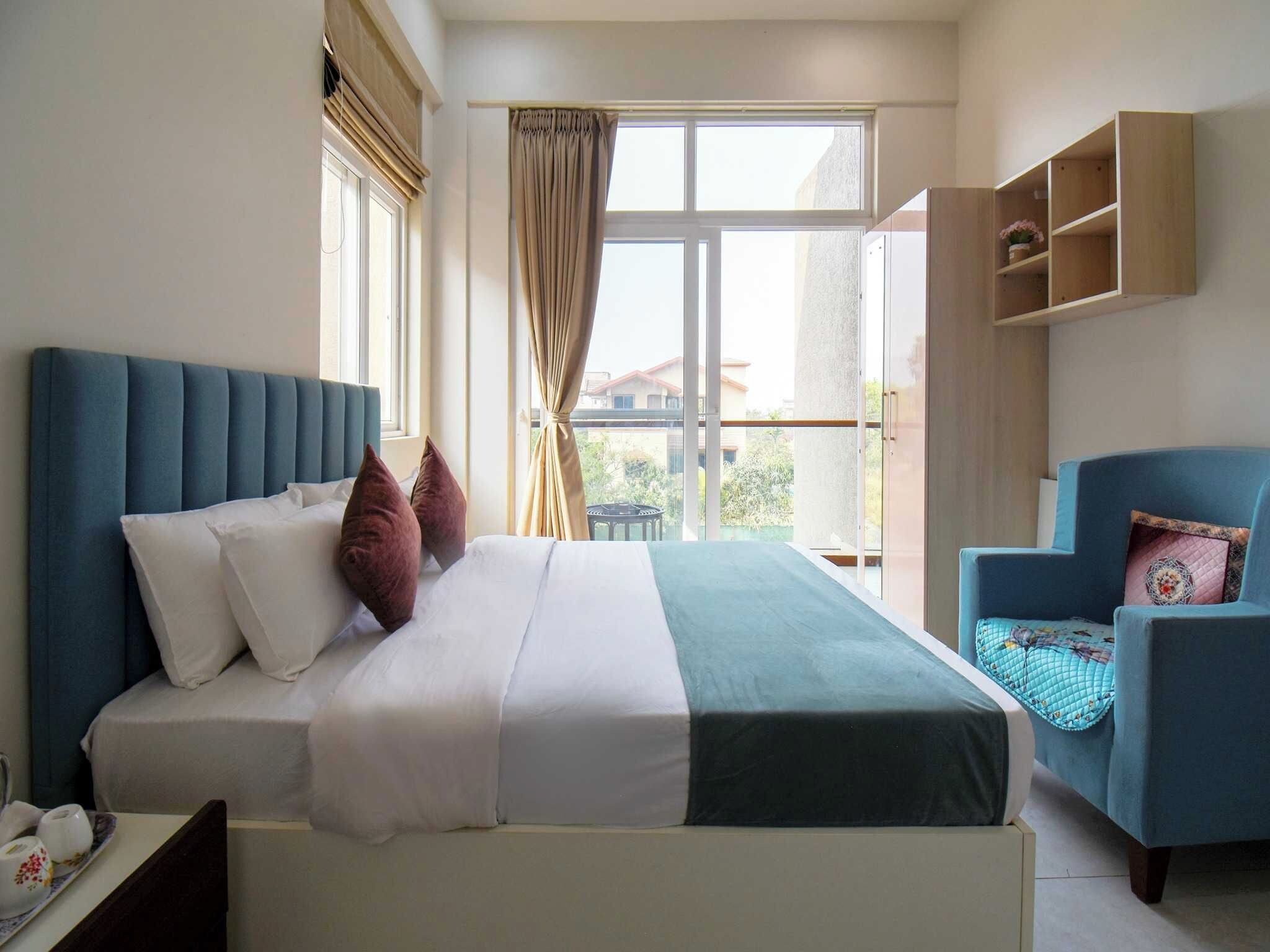 A hotel room with a bed, a chair, and a view of the outside.
