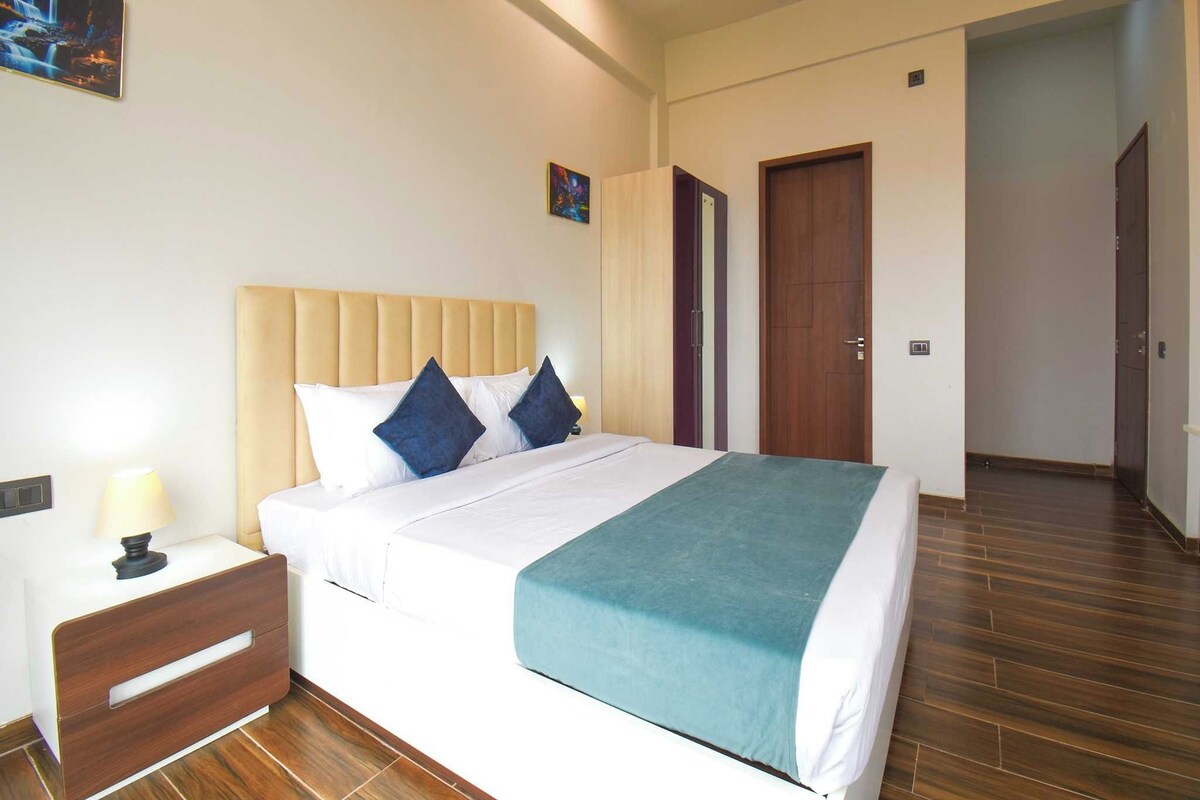 A hotel room with a bed, bedside table, lamp, and a door leading to another room.