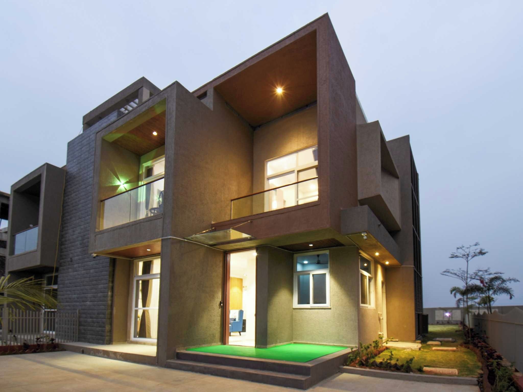 A modern two-story residential building with a flat roof, large windows, and a green lawn in front.