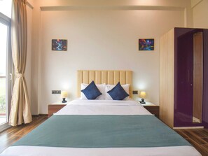 A hotel room with a large bed, two bedside tables with lamps, a headboard, and two paintings on the walls.