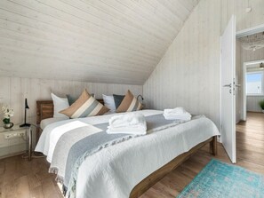 A bedroom with a sloped ceiling, a bed with a striped blanket, a bedside table with a lamp, and a view of the outdoors through an open door. - NEW - Beach Lodge (Kappeln)