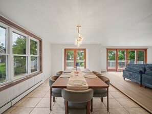 A spacious dining area with a long table and chairs, a chandelier, and large windows offering a view of the outdoors. - Point Gratiot Lake House, Sleeps 12+, Lake Views (Dunkirk)