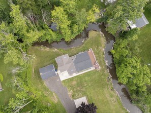 An aerial view of a house with a large deck, surrounded by trees and a small stream. - Point Gratiot Lake House, Sleeps 12+, Lake Views (Dunkirk)
