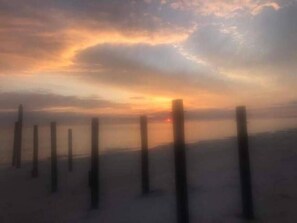 Ein Strandbild mit Holzpfählen und einem Sonnenuntergang im Hintergrund.