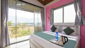 Quarto de hotel com uma cama grande, vista para o campo e parede rosa.