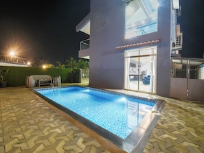Une piscine dont le bord est revêtu de carreaux, entourée d’une zone pavée avec un motif en chevrons.