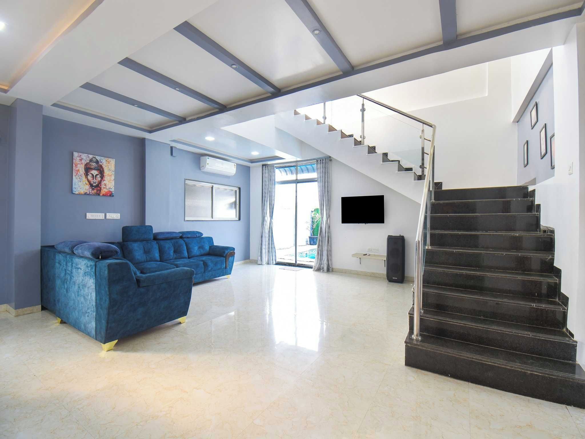 Amplia sala de estar con un conjunto de sofá azul, una escalera y un televisor de pantalla plana montado en la pared.