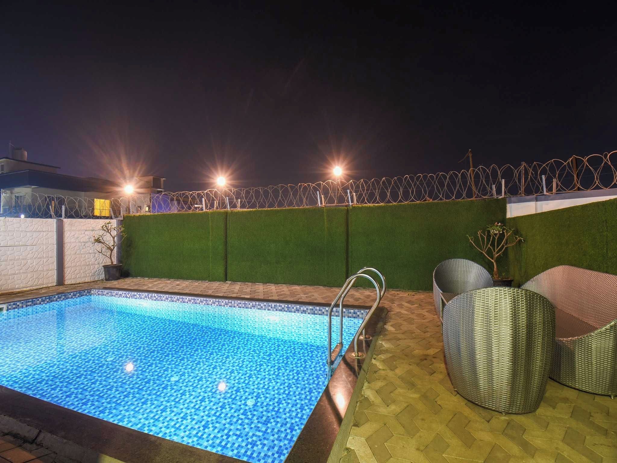 A swimming pool with a tiled edge, surrounded by a low wall with barbed wire, and outdoor furniture.