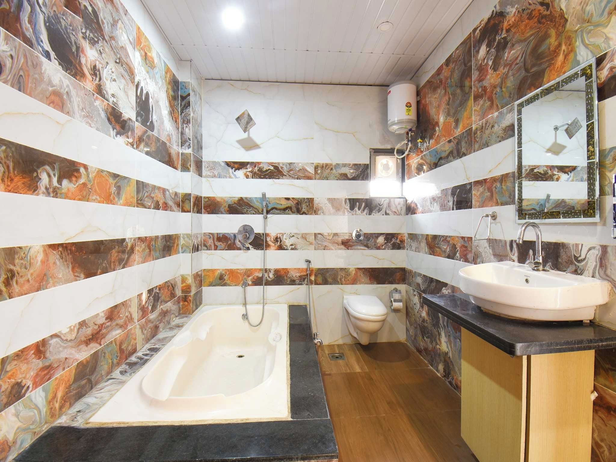 A bathroom with a bathtub, toilet, and sink, featuring marble-like wall tiles and a wooden floor.