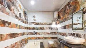 Casa de banho com banheira, sanita e lavatório, com azulejos de aspeto marmorizado e chão em madeira.
