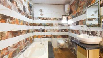 A bathroom with a bathtub, toilet, and sink, featuring marble-like wall tiles and a wooden floor.