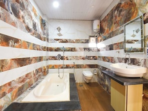 A bathroom with a bathtub, toilet, and sink, featuring marble-like wall tiles and a wooden floor. - DanCenter Arohi Villa 4BHK Pvt Pool (Mawal)