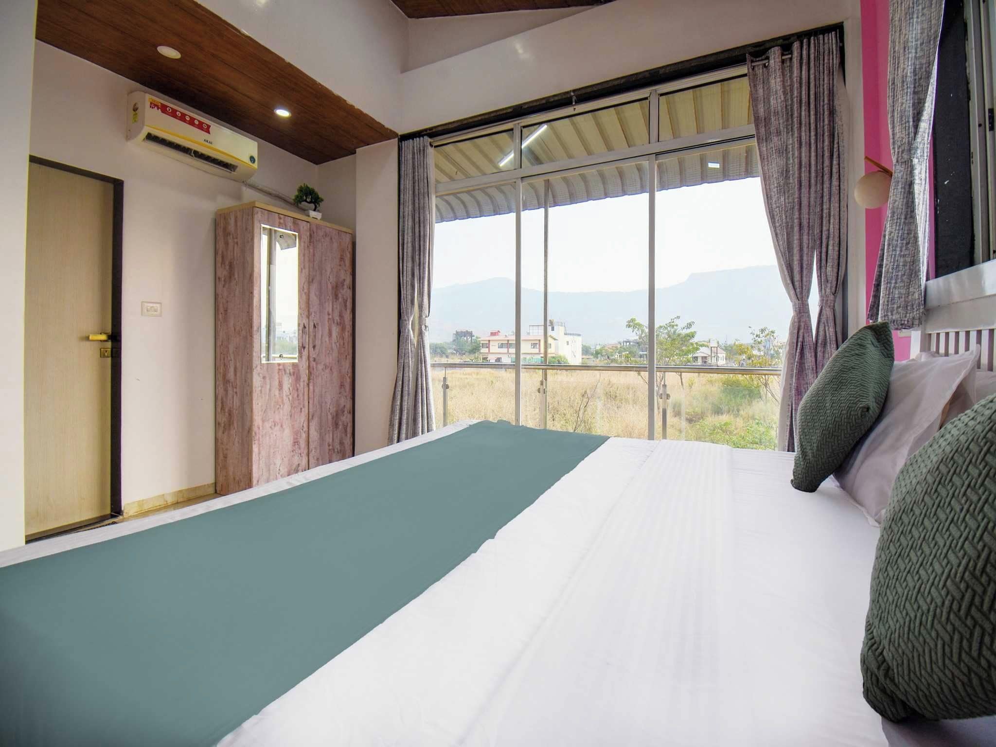 A bedroom with a large bed, a wardrobe, and a window with a view of buildings and mountains.