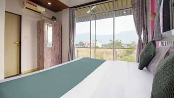 A bedroom with a large bed, a wardrobe, and a window with a view of buildings and mountains.