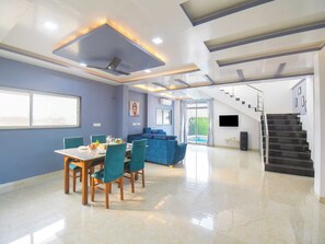 A modern interior with a dining area, sofa, staircase, and a view of the outdoors. - DanCenter Arohi Villa 4BHK Pvt Pool (Mawal)