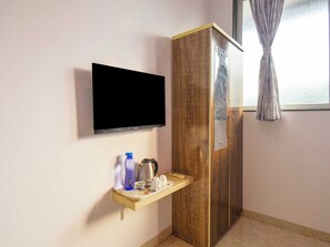 A room with a flat-screen TV mounted on the wall, a wooden wardrobe, and a small shelf with a kettle, cups, and bottles. - DanCenter Arohi Villa 4BHK Pvt Pool (Mawal)