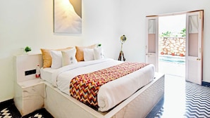 Quarto de hotel com cama, mesas de cabeceira, luminária na parede, ventoinha no teto e porta aberta para área externa.