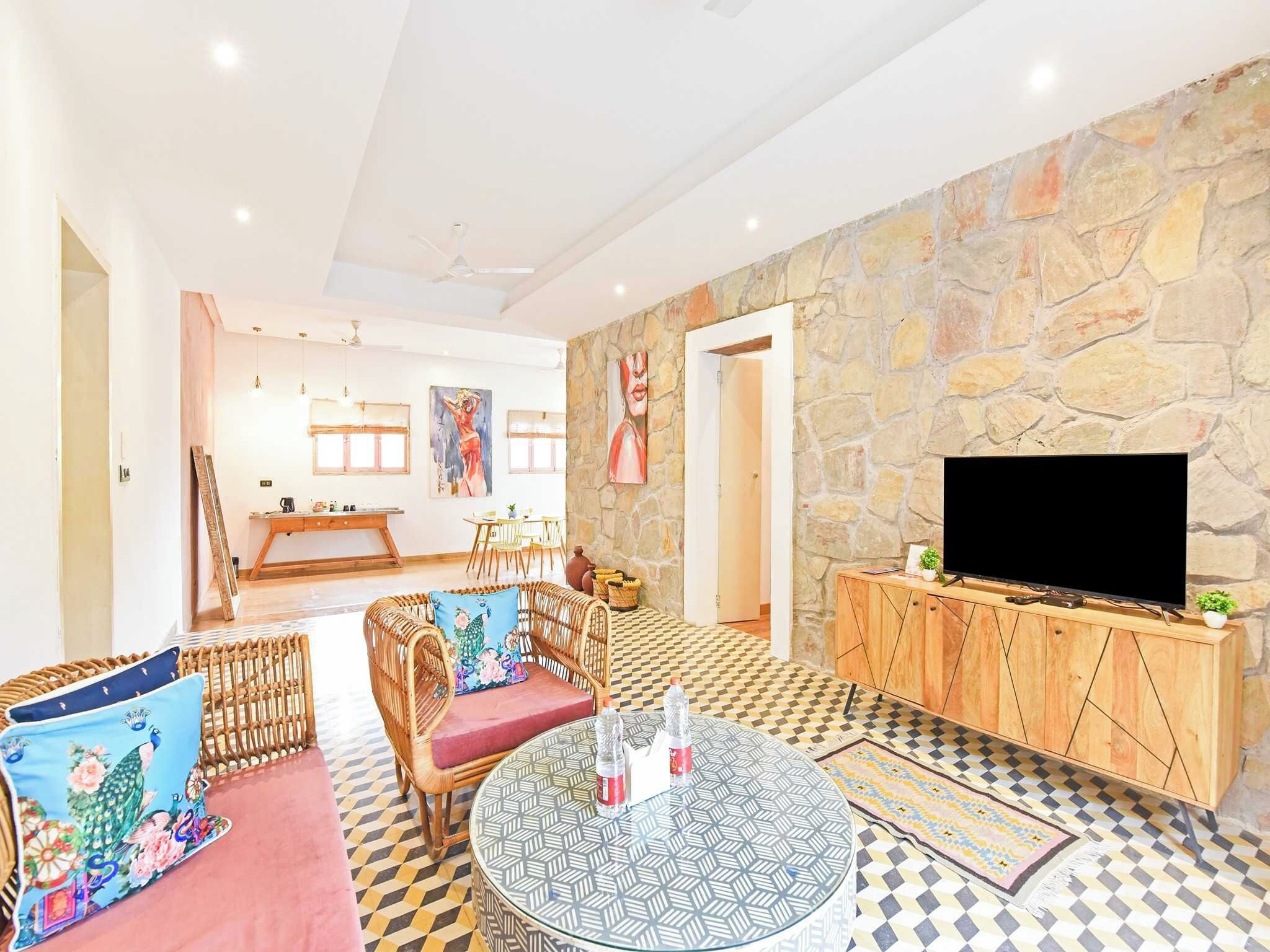 Amplia sala de estar con pared de piedra, televisor y comedor con sillas y mesa.