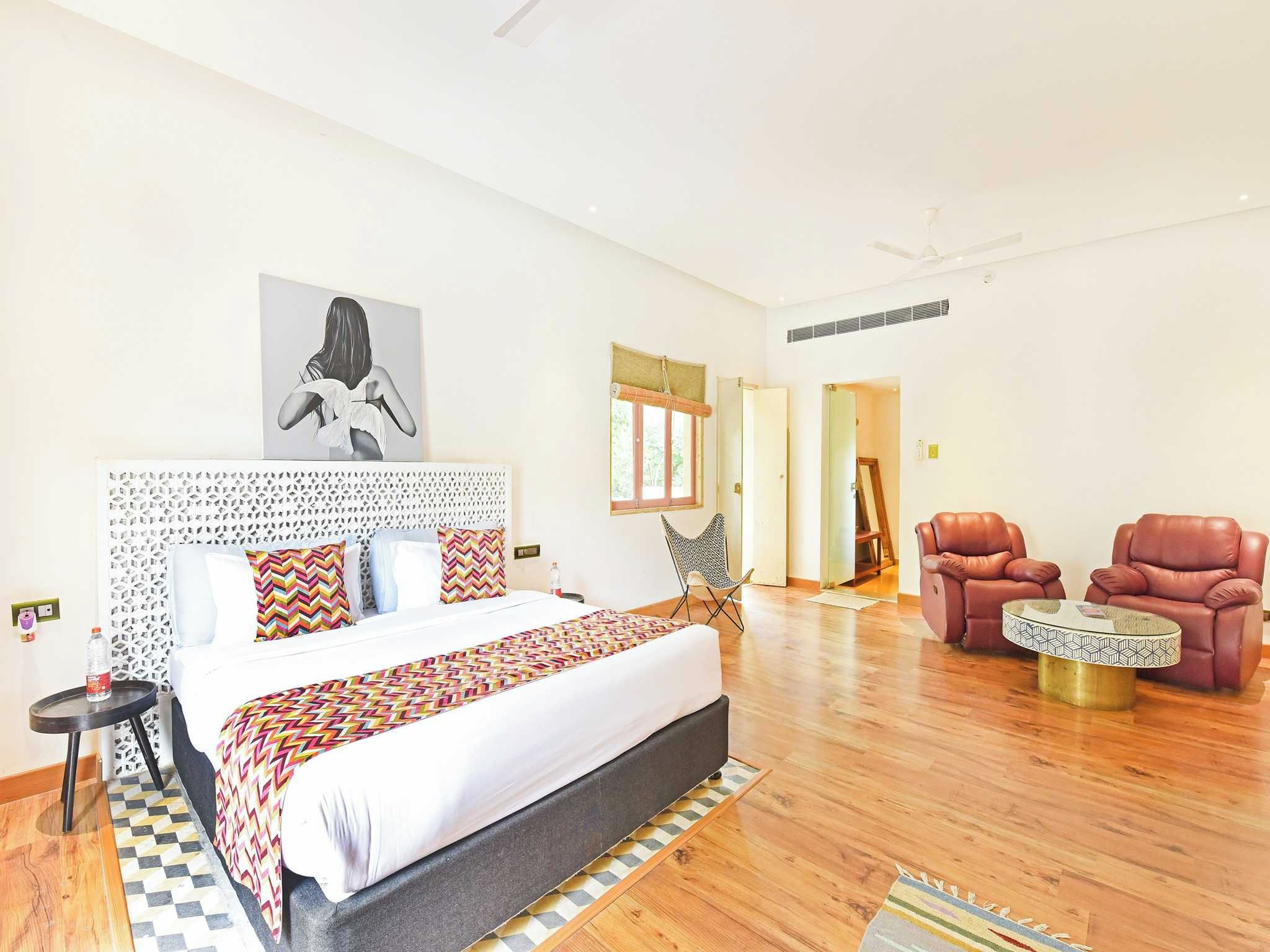 Habitación de hotel con una cama grande, una zona de estar con dos sillas, una mesita y una ventana con vistas.
