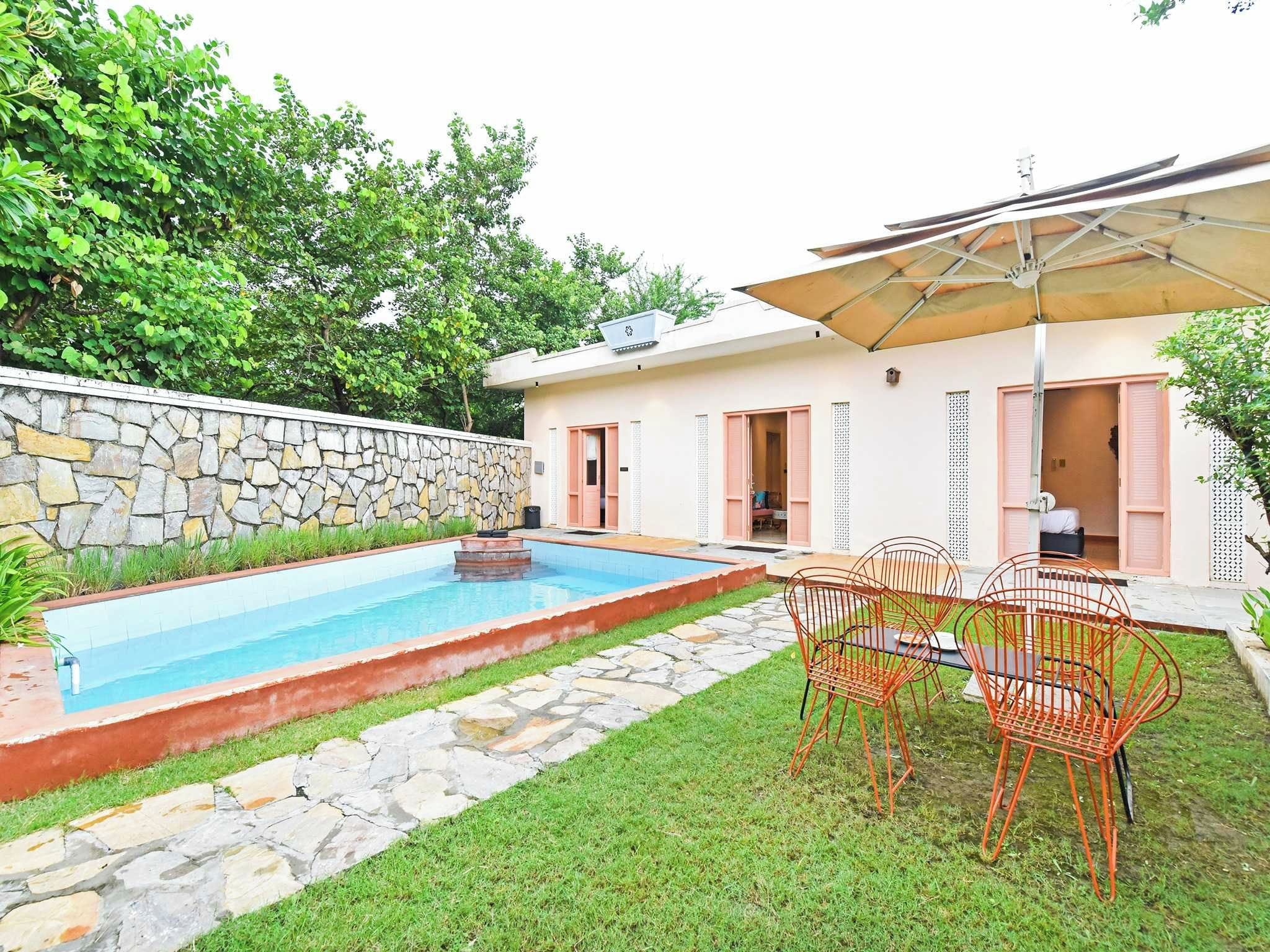 A swimming pool with a stone border, a stone wall, and a grassy area with outdoor furniture.