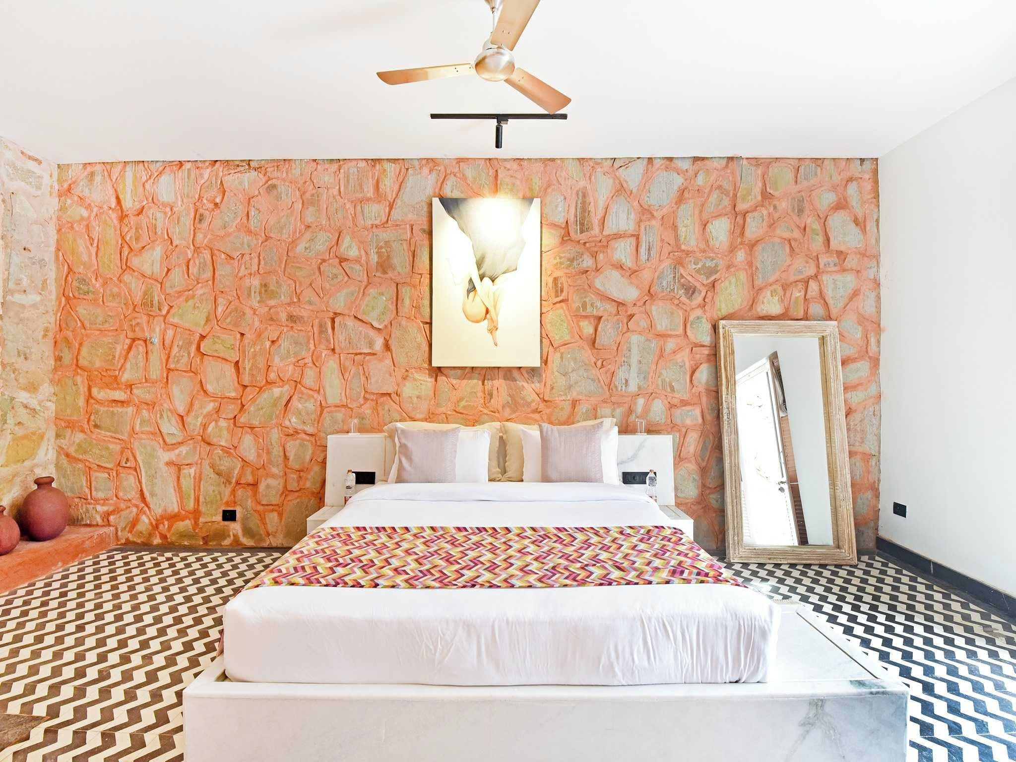 Una habitación de hotel con una cama, un ventilador de techo, una pared con diseño de piedra y un espejo.
