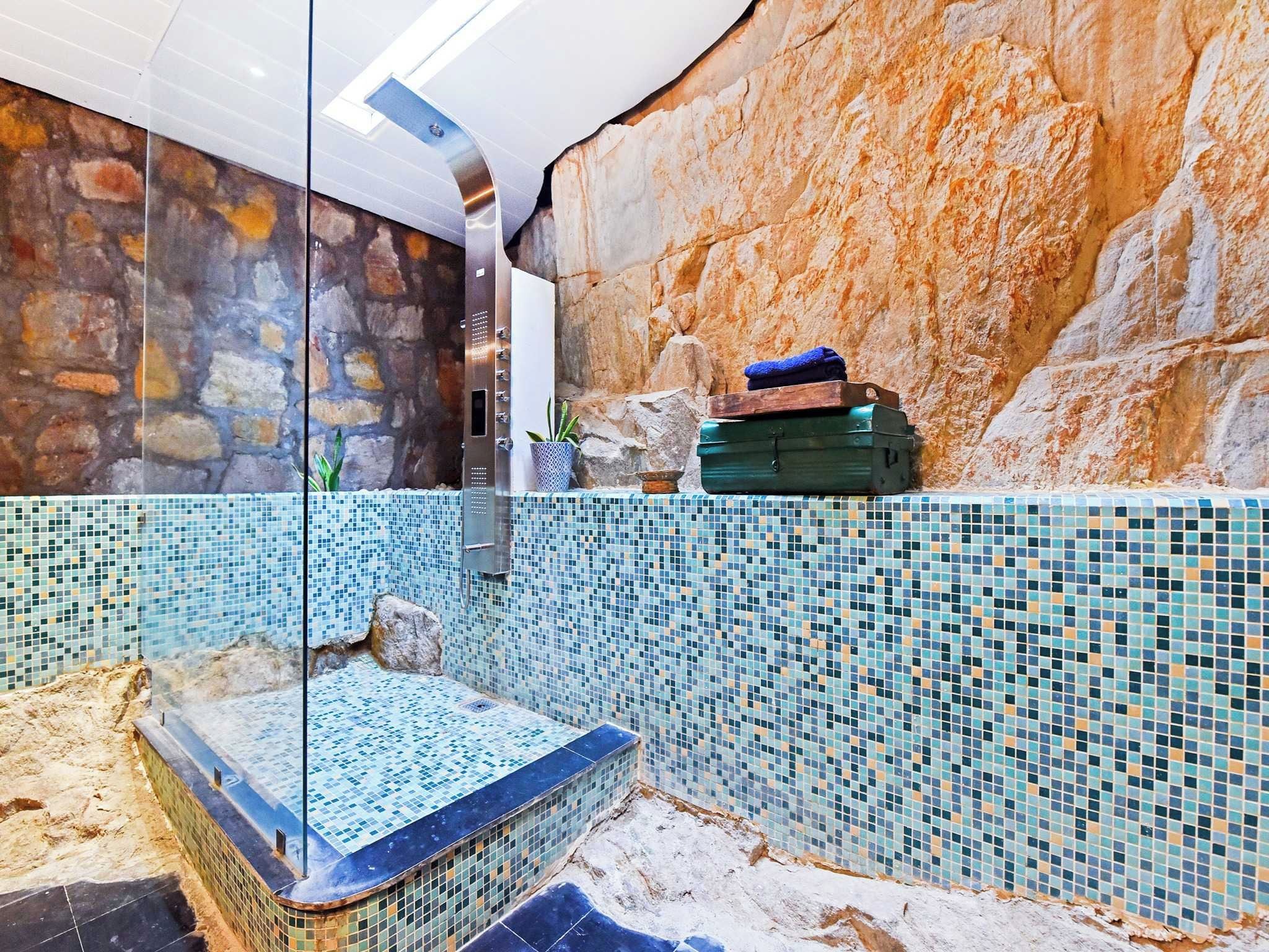 Un área de spa con pared de mosaicos, pared de piedra y bañera de hidromasaje con recinto de vidrio.