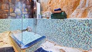 Uma área de spa com parede revestida de mosaico, parede de pedra e banheira de hidromassagem com isolamento de vidro.