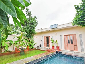 Una propiedad residencial con piscina, un patio cubierto y un jardín con plantas en macetas.